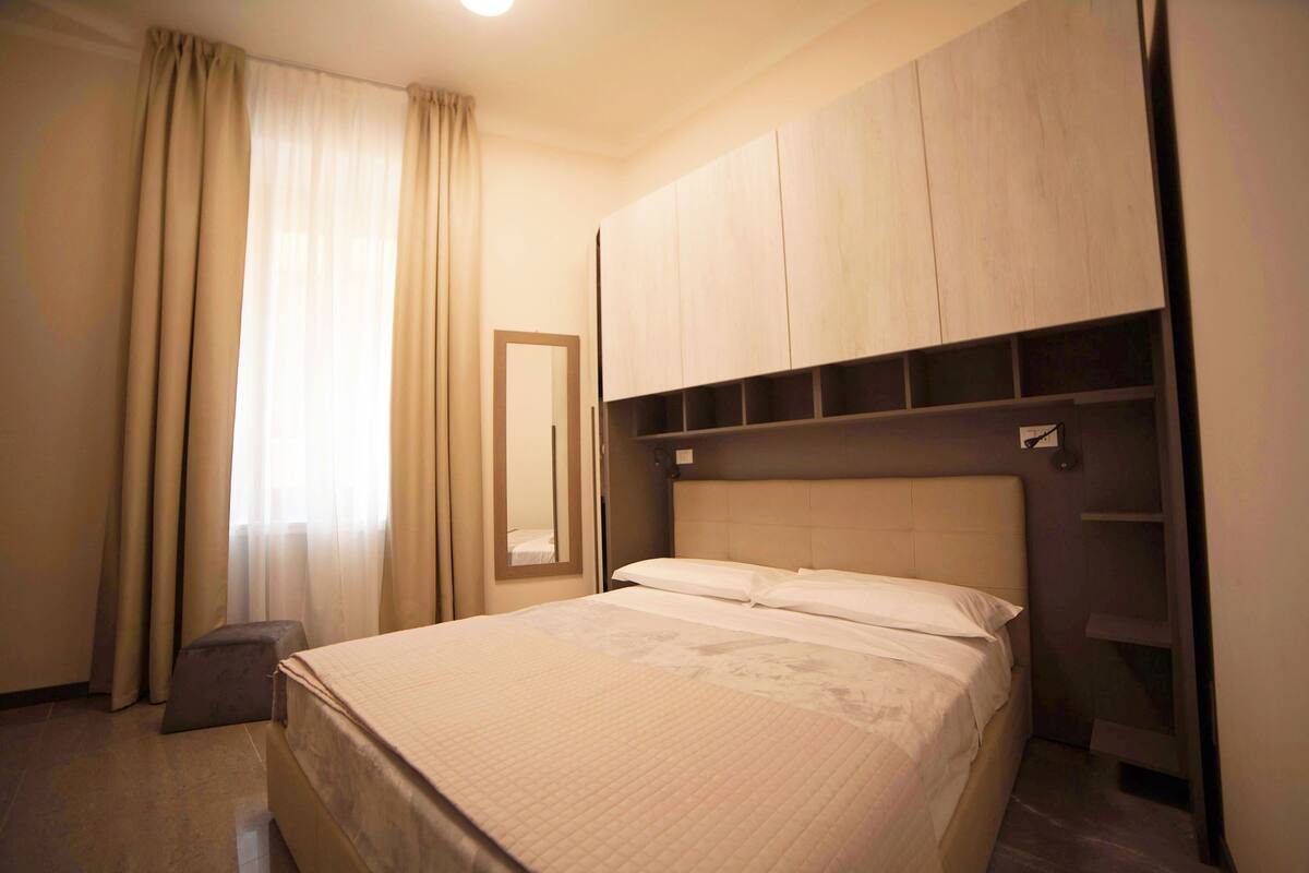 A hotel room with a bed, a wardrobe, a small stool, and a mirror.