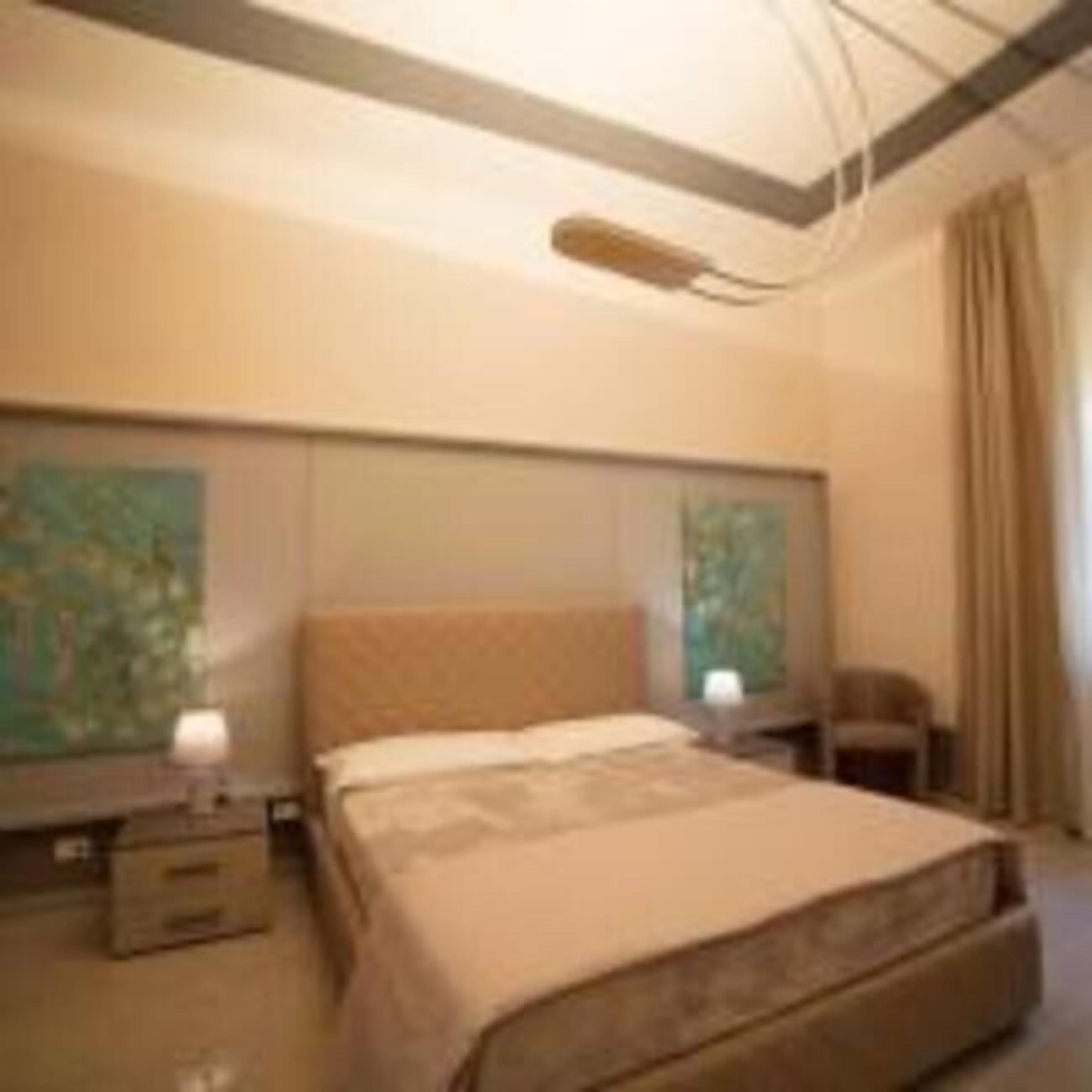 A bedroom with a large bed, a nightstand, a lamp, and a painting on the wall.