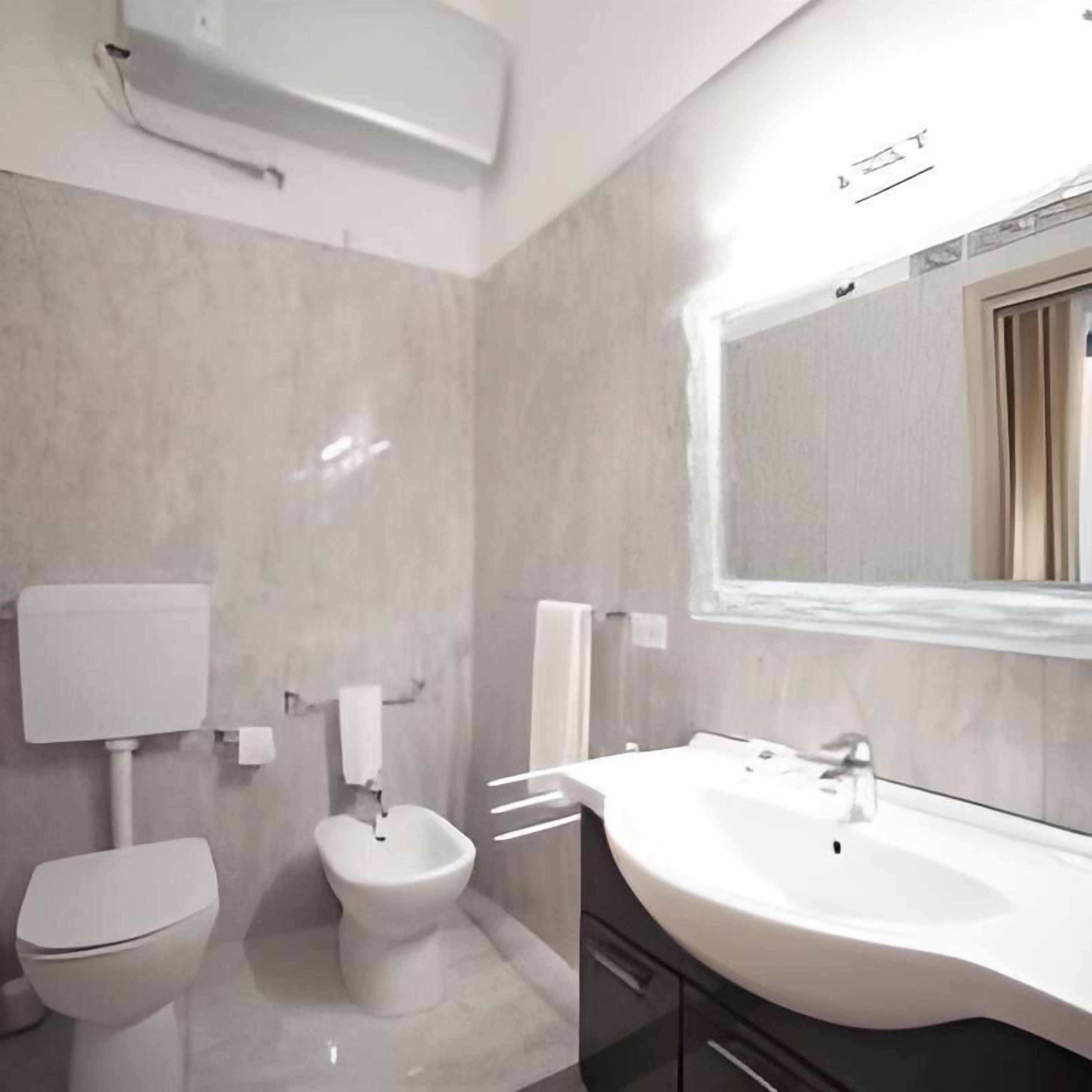 A modern bathroom with a toilet, bidet, and a large sink with a mirror above it.