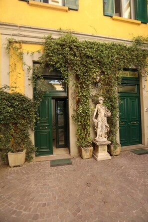 A building facade with green doors, a statue, and potted plants. - IMHOME - Cadorna House (Milan)