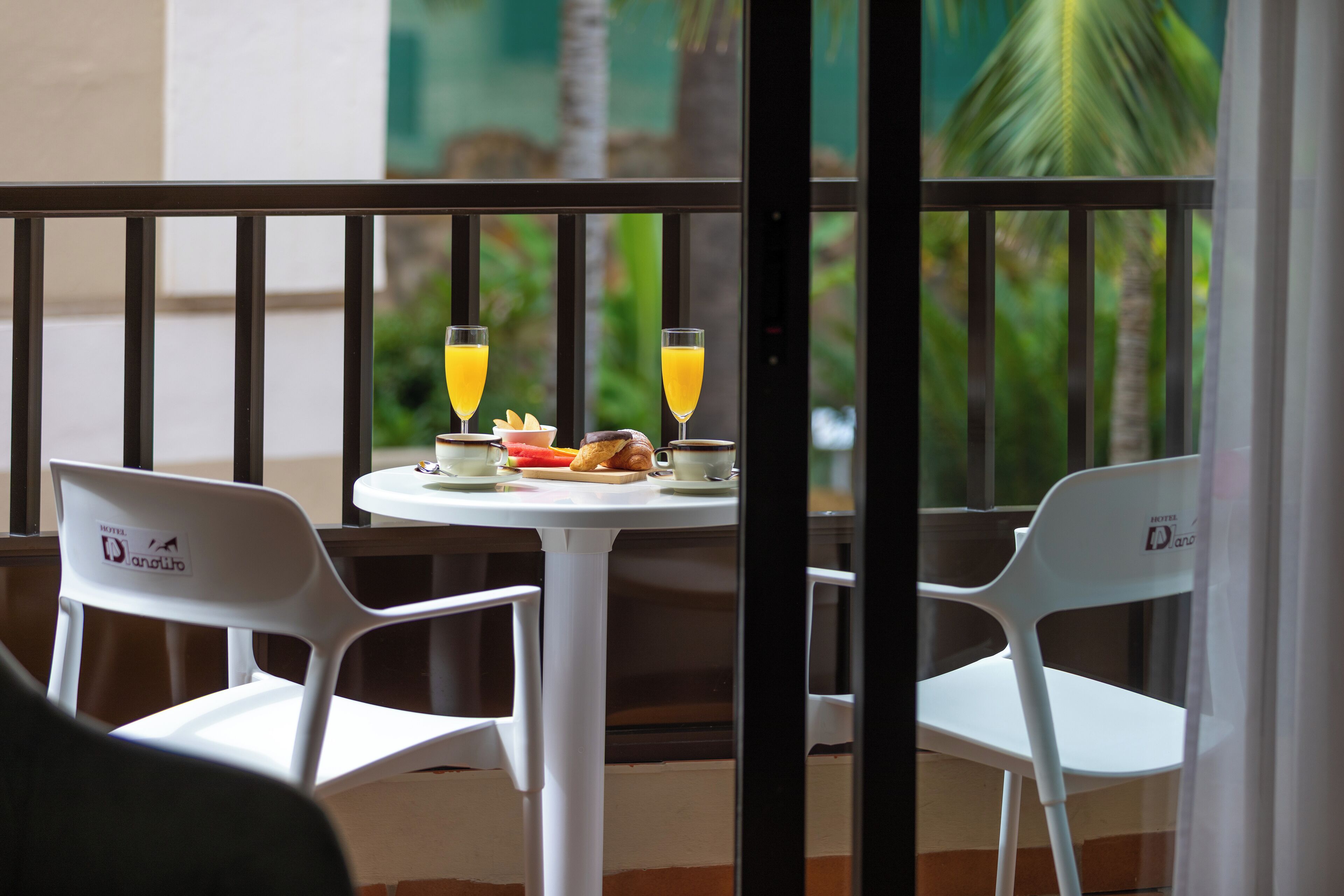 A balcony with two white chairs, a small round table, and a glass of orange juice.