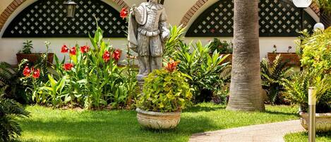 A statue in a garden with a pathway, surrounded by various plants and flowers.