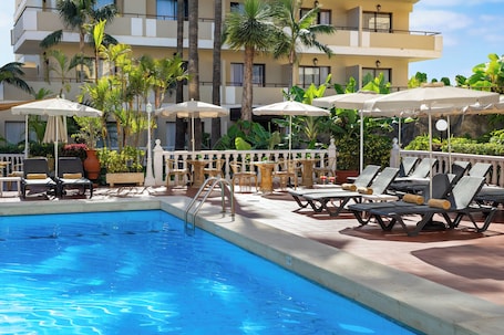 Una piscina al aire libre, sombrillas, sillones reclinables de piscina