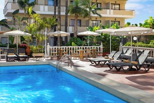 Una piscina al aire libre, sombrillas, sillones reclinables de piscina