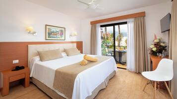 Une chambre d’hôtel avec un grand lit, une table de chevet, une chaise, un ventilateur de plafond, une télévision et un balcon équipé d’une table et de chaises.