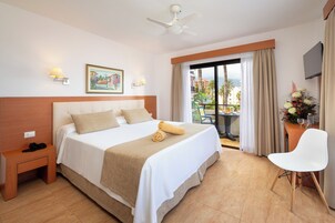 Une chambre d’hôtel avec un grand lit, une table de chevet, une chaise, un ventilateur de plafond, une télévision et un balcon équipé d’une table et de chaises.