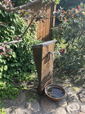 Un élément décoratif extérieur de style rustique, composé d’une structure en bois, d’un bec verseur en métal et d’un bassin rempli d’eau.