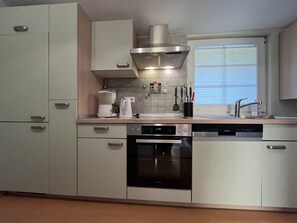 Une cuisine moderne équipée d’appareils électroménagers en acier inoxydable, d’un lave-vaisselle et d’une fenêtre avec des stores.