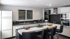 A modern kitchen with a central island, black bar stools, and built-in appliances.