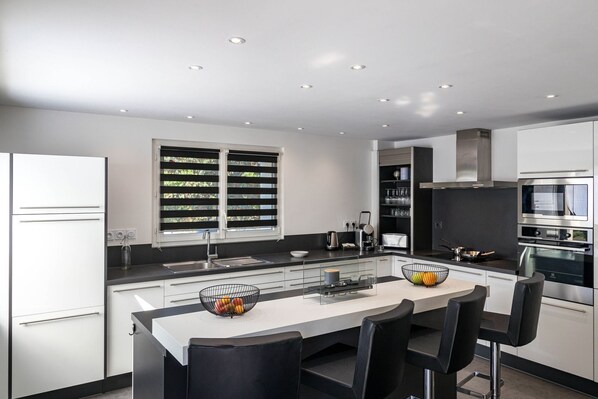 A modern kitchen with a central island, black bar stools, and built-in appliances.