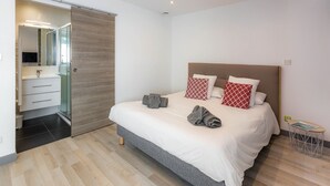 A modern bedroom with a large bed, a walk-in closet, and a bathroom with a glass shower.