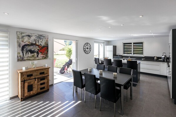 A modern kitchen with a dining area, large windows, and a clock on the wall. - Emma's Villa in Crots (Crots)