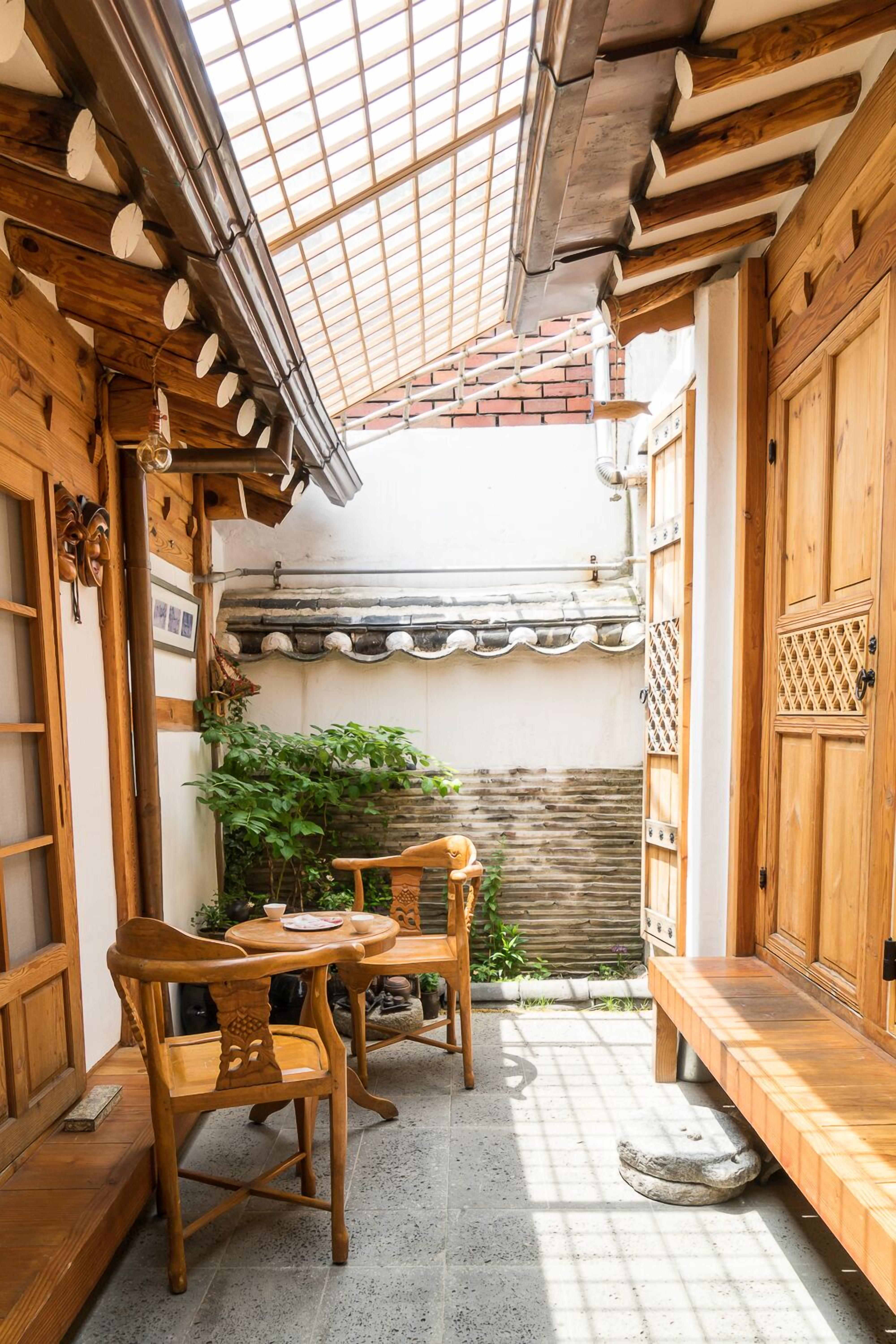 A traditional Japanese-style courtyard with wooden furniture, a stone floor, and a tiled roof.