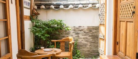 A traditional Japanese-style courtyard with wooden furniture, a stone floor, and a tiled roof.