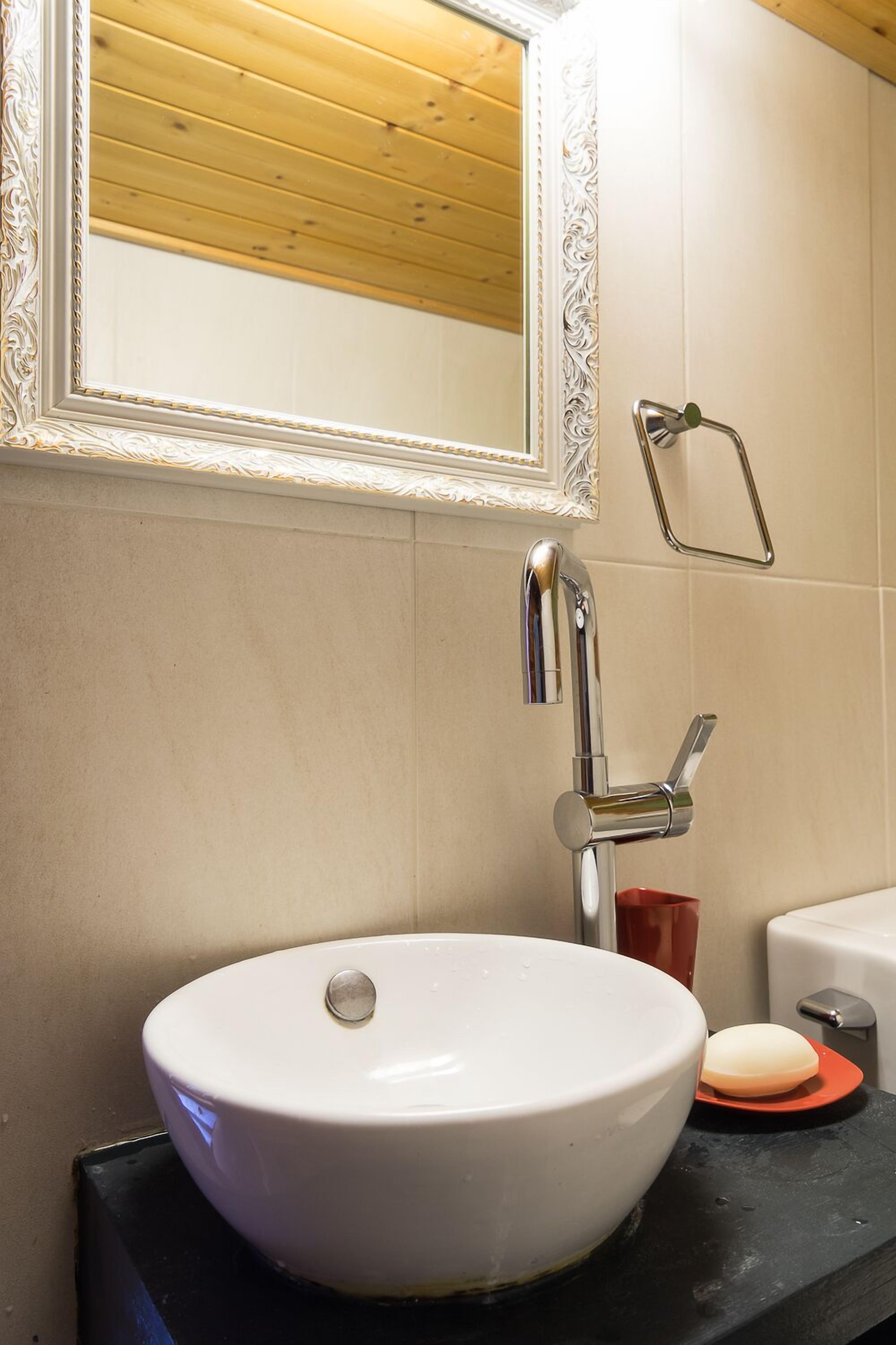 A bathroom with a white sink, a chrome faucet, a mirror with an ornate frame, and a towel rack.