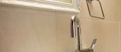 Un baño con un lavamanos blanco, un grifo cromado, un espejo con un marco decorativo y un perchero para toallas.