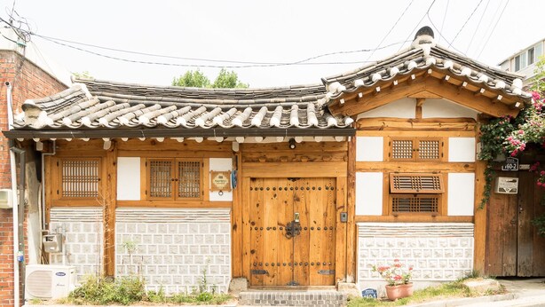 Edificio japonés tradicional con puerta de madera, tejado de tejas y un pequeño jardín con plantas en macetas.