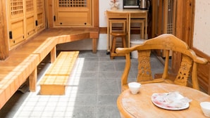 Un interior de madera tradicional con un esterilla de tatami, una mesa de madera con un plato y un cuenco, y una zona de cocina con microondas y hervidor.