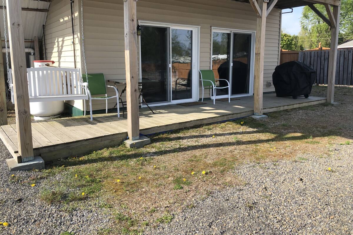 A covered patio with a wooden deck, a grill, and a barbecue.