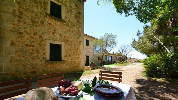 A rustic stone building with a table set for a meal, featuring bread, grapes, and a plate. - Son Palanca, Finca 5starshome Mallorca (Sineu)