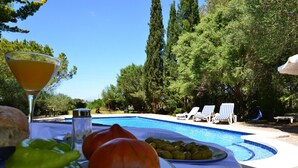 A poolside setting with a table set for breakfast, including bread, tomatoes, olives, and a glass of orange juice. - Son Palanca, Finca 5starshome Mallorca (Sineu)