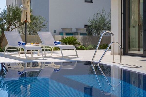 Zona de piscina con sillas de descanso y una escalera metálica.