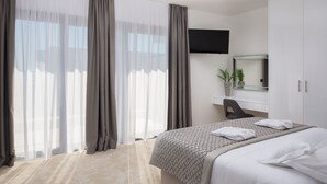 Hotellihuone, jossa on sänky, työpöytä, tuoli, televisio ja suuri ikkuna, jossa on verhot.