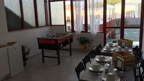 A dining area with a foosball table, a table set for a meal, and large windows with curtains.