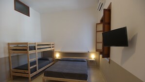 A room with two bunk beds, a flat bed, a TV mounted on the wall, and a small table.