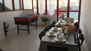 A dining area with a foosball table, a table set for four, and large windows with red frames.