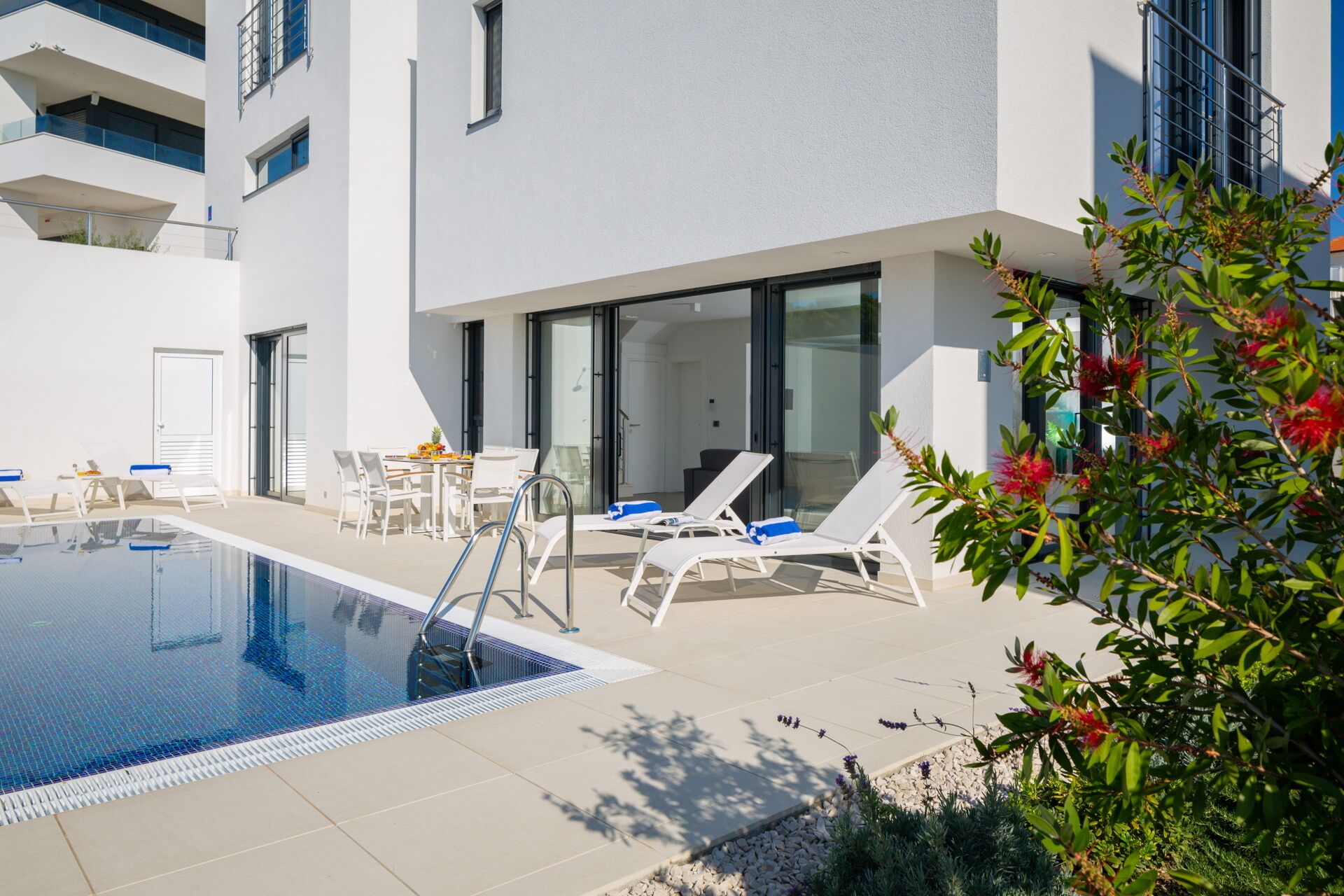 Ein moderner Poolbereich im Freien mit Liegestühlen, einem Esstisch und freiem Blick auf die Außenfassade des Gebäudes.