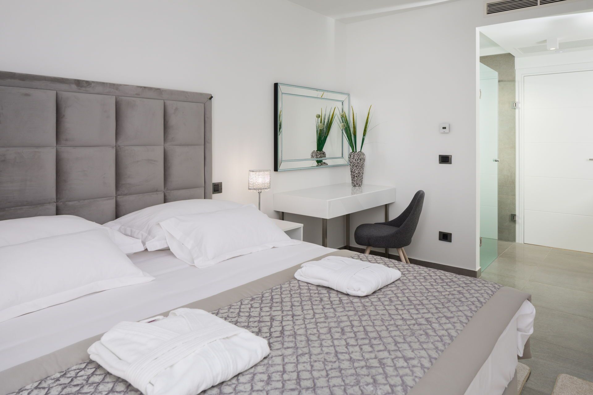 A modern hotel room with a large bed, a desk, a chair, and a bathroom visible through an open door.