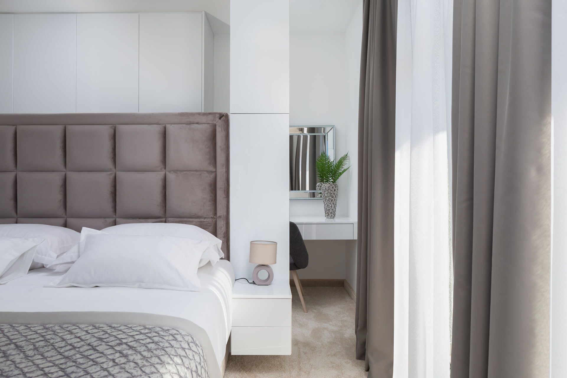 Een moderne hotelkamer met een groot bed, een nachtkastje met een lamp, een bureau met een stoel en een plant in een pot.
