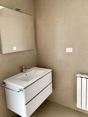 A bathroom with a white vanity, a mirror, and a radiator. - Ambasciatori B&B (Catania)