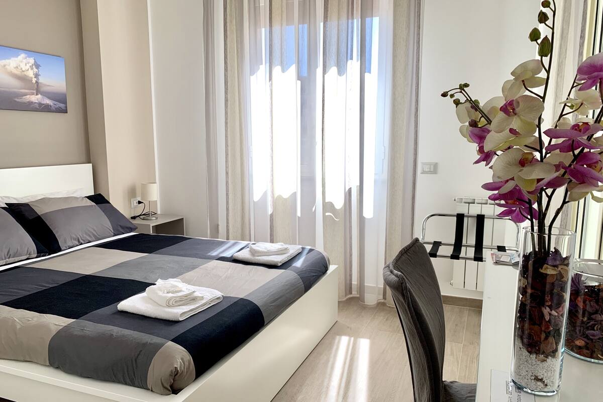 A modern hotel room with a large bed, a desk, and a vase of flowers.