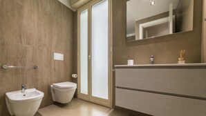 A modern bathroom with a bidet, toilet, and vanity with a mirror. - Ambasciatori B&B (Catania)
