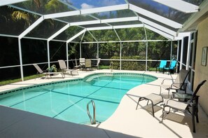A covered swimming pool with lounge chairs and a glass enclosure. - Cape_escape (Cape Coral)