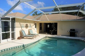 A swimming pool with a covered patio area, two lounge chairs, and a grill. - Cape_escape (Cape Coral)
