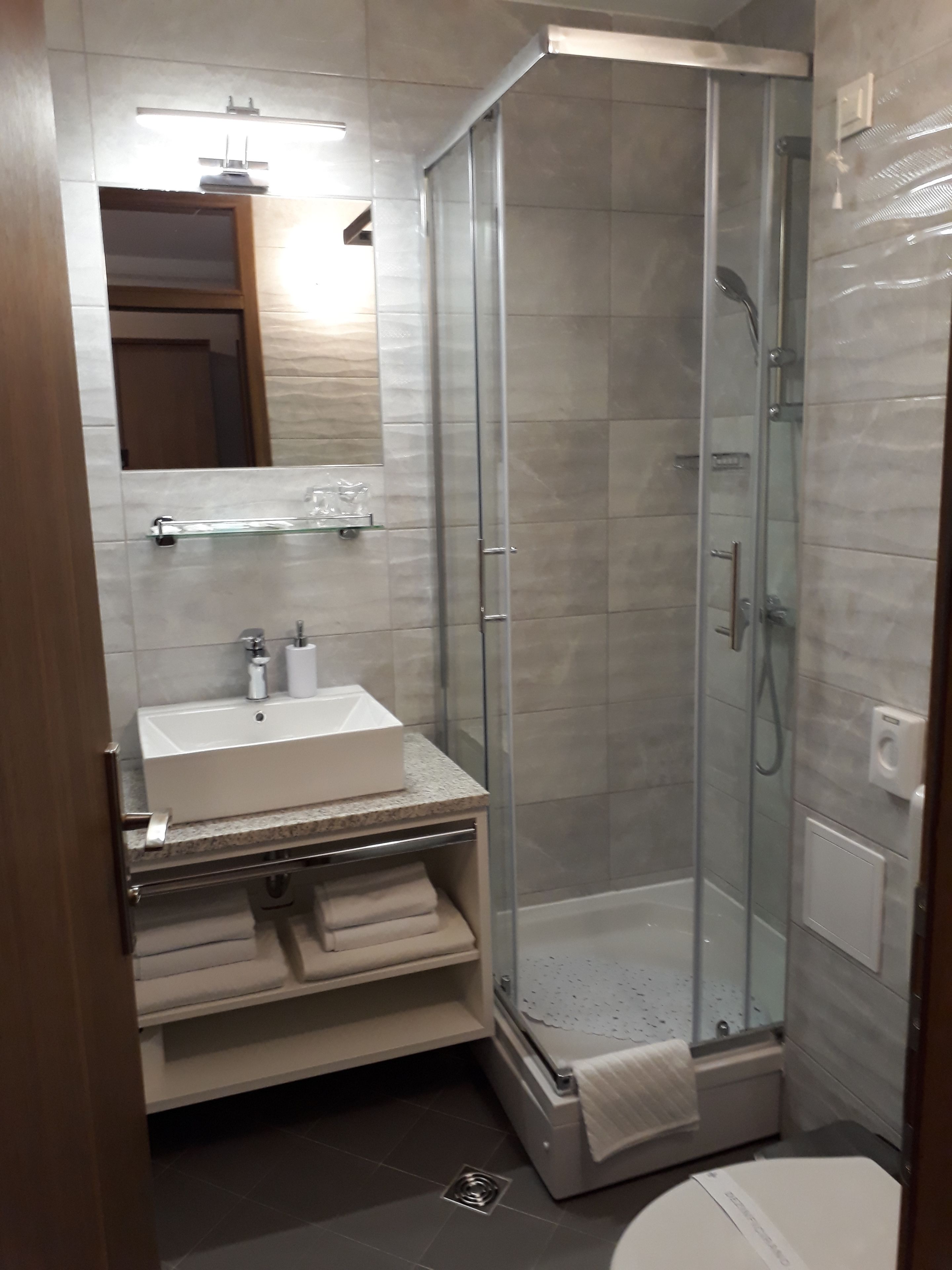 A modern bathroom with a glass-enclosed shower, a white sink with a marble countertop, and a mirror above the sink.