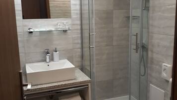 A modern bathroom with a glass-enclosed shower, a white sink with a marble countertop, and a mirror above the sink.