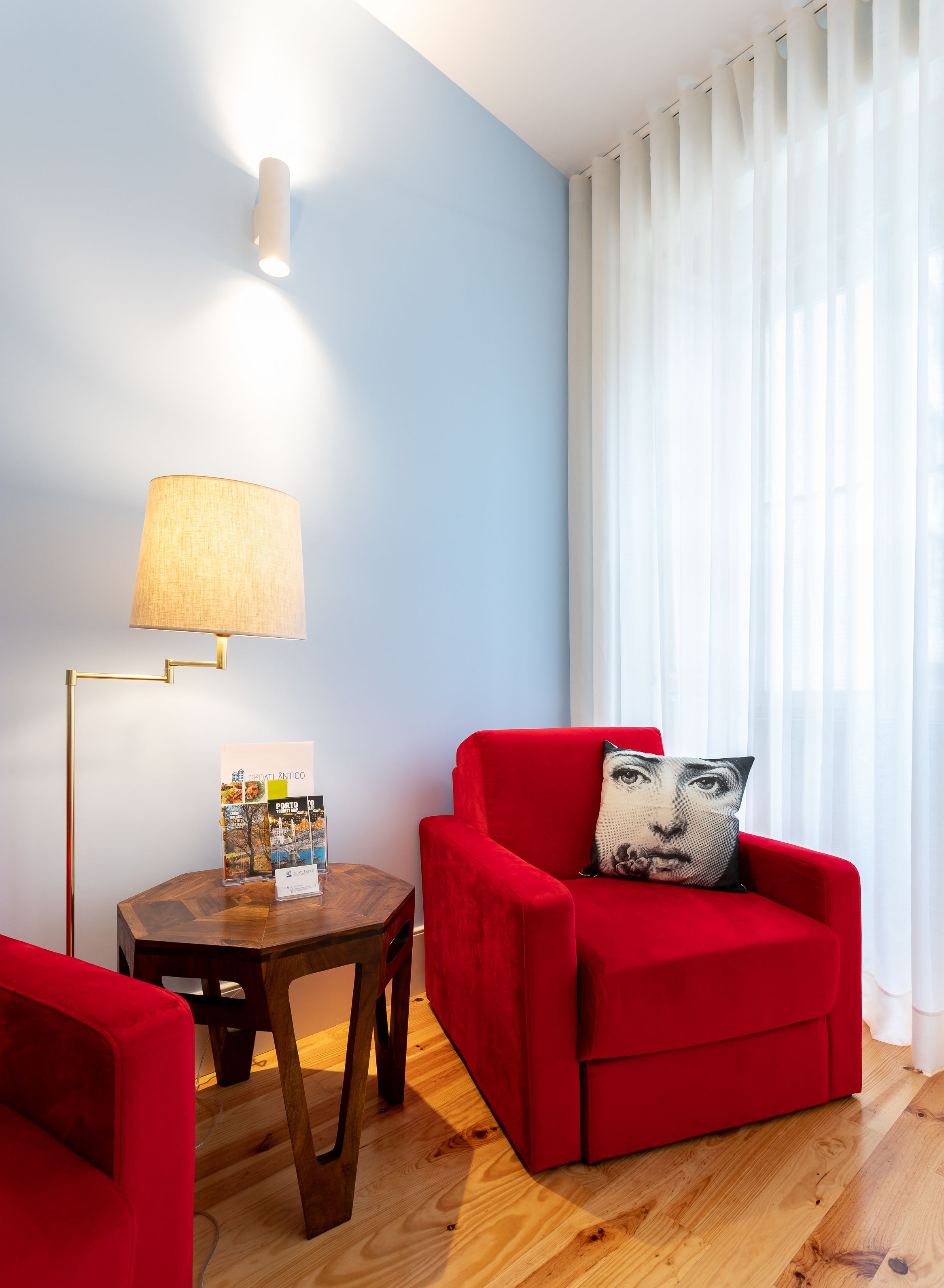 A modern living room with a red armchair, a round wooden side table, and a floor lamp.