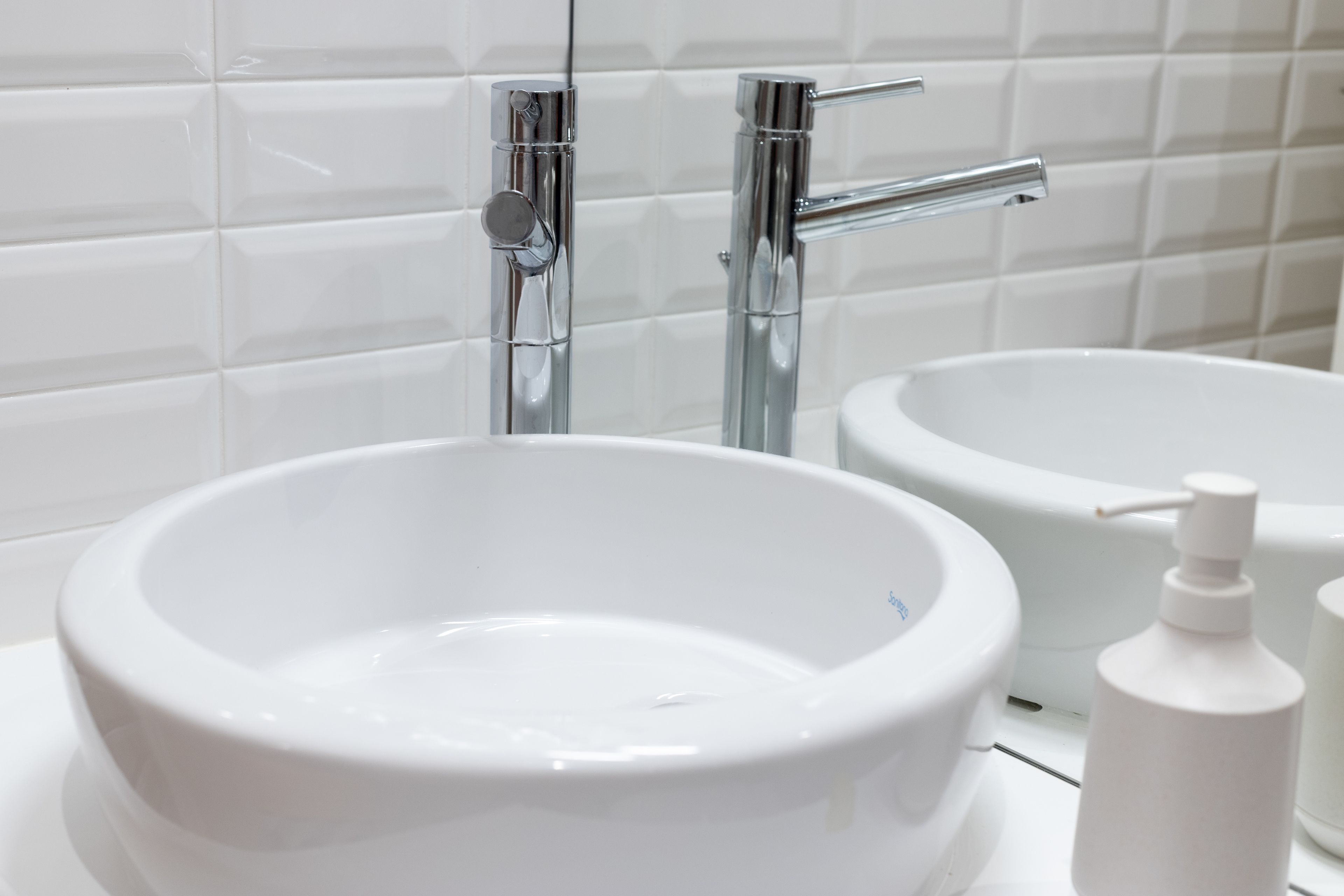 A bathroom with a white sink, a mirror, and a chrome faucet.