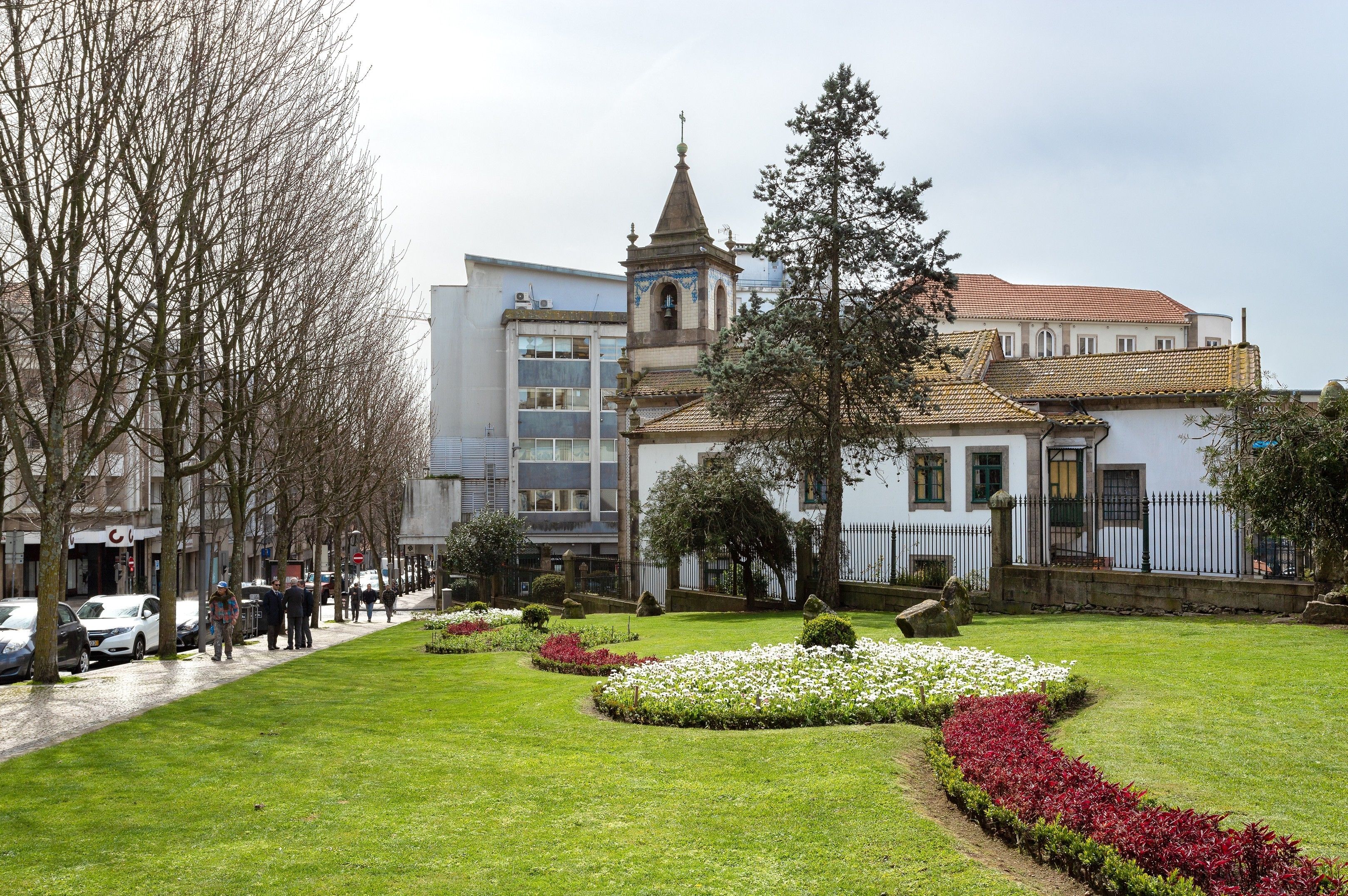 A building with a tower, surrounded by a well-maintained garden with various plants and flowers.