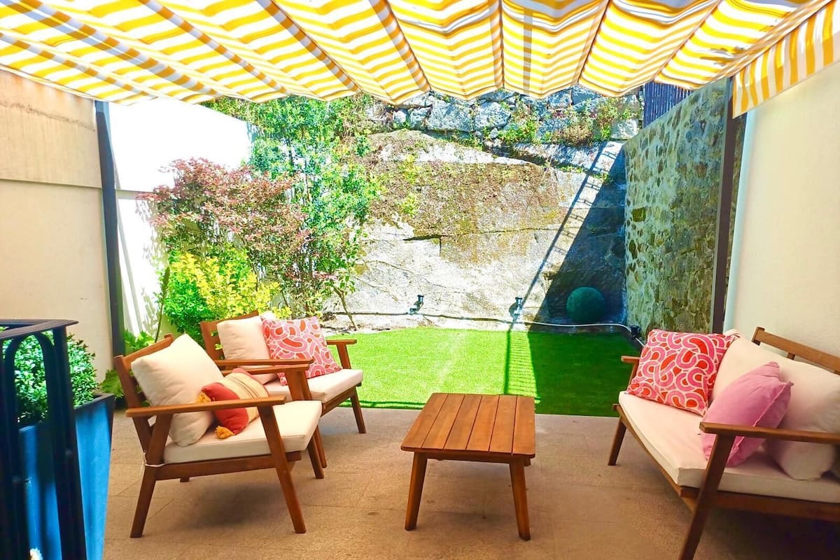 Un patio con mobiliario de madera, una pequeña mesa y un toldo a rayas amarillas.
