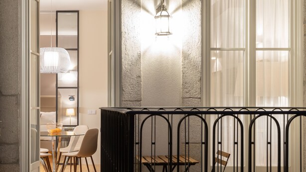 En modern interiör med en glasdörr som leder till en matplats, ett svart metallstaket och en vägg med en intressant struktur, samt en väggmonterad lampa.