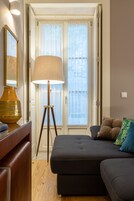 Quarto com sofá de cor escura, luminária de chão e mesa lateral de madeira.