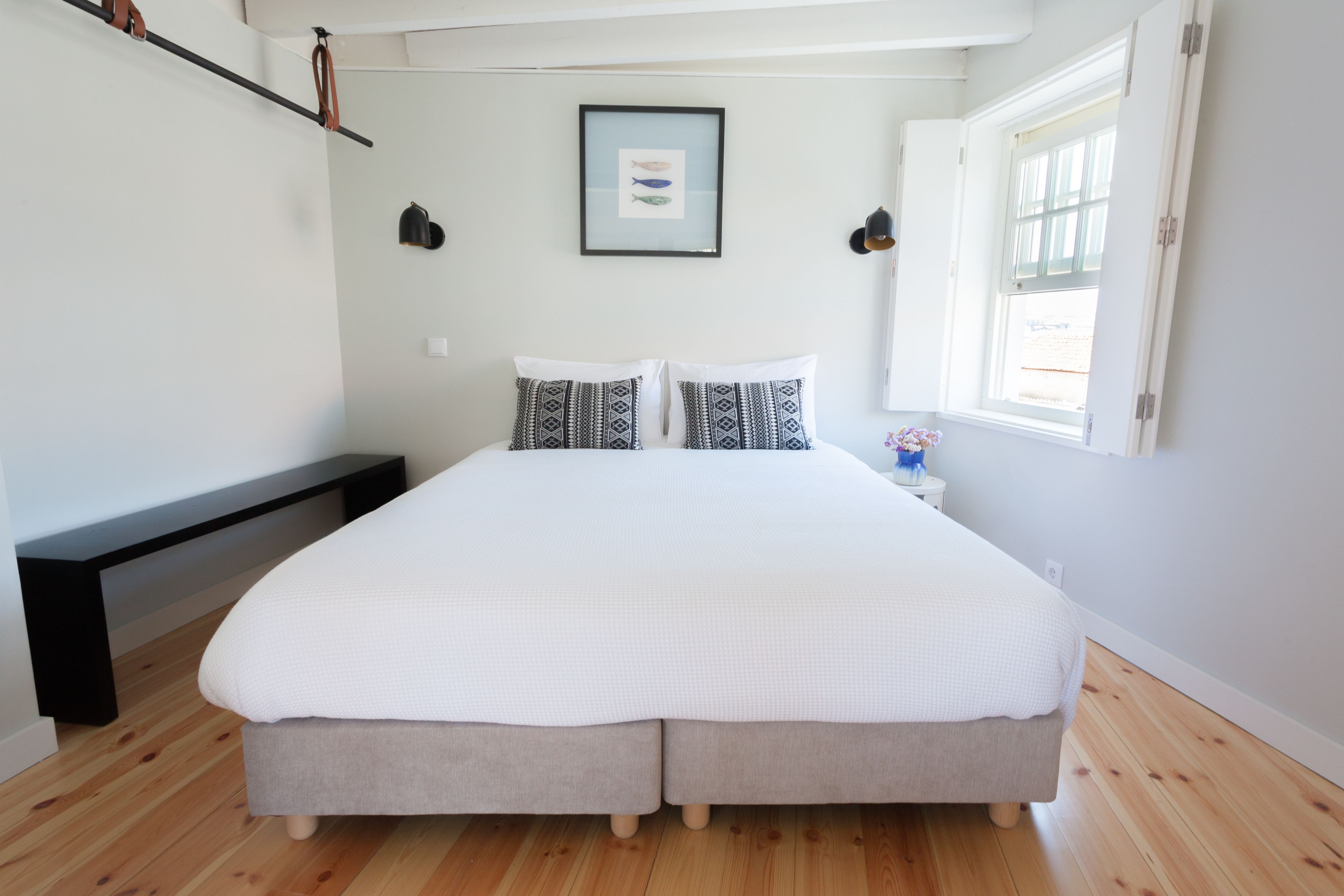 Un dormitorio con una cama grande, una mesita de noche con lámpara, un cuadro en la pared y una ventana con cortinas.
