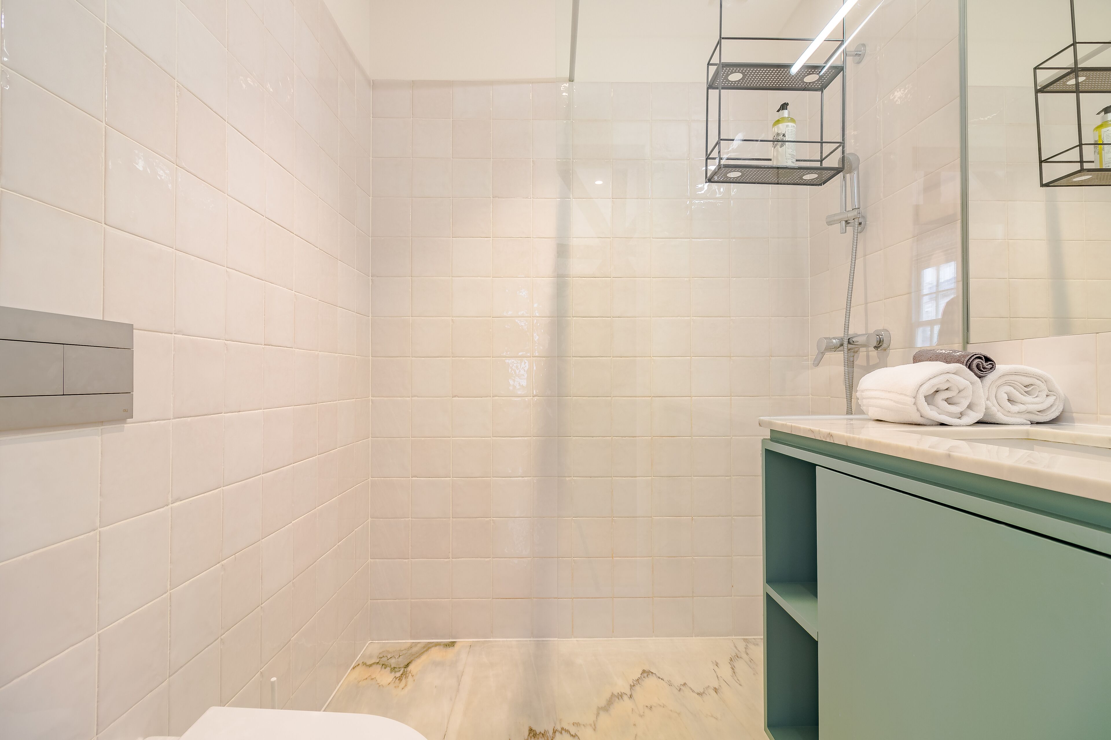 Un baño moderno con azulejos blancos, cabina de ducha de vidrio y un mueble de tocador verde con toallas.