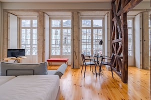 Een hotelkamer met een bed, een bureau met stoel, een televisie en grote ramen met uitzicht op gebouwen.