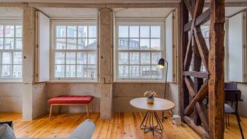 A room with large windows, a wooden floor, a round table with a vase, a bench, and a wooden beam structure.